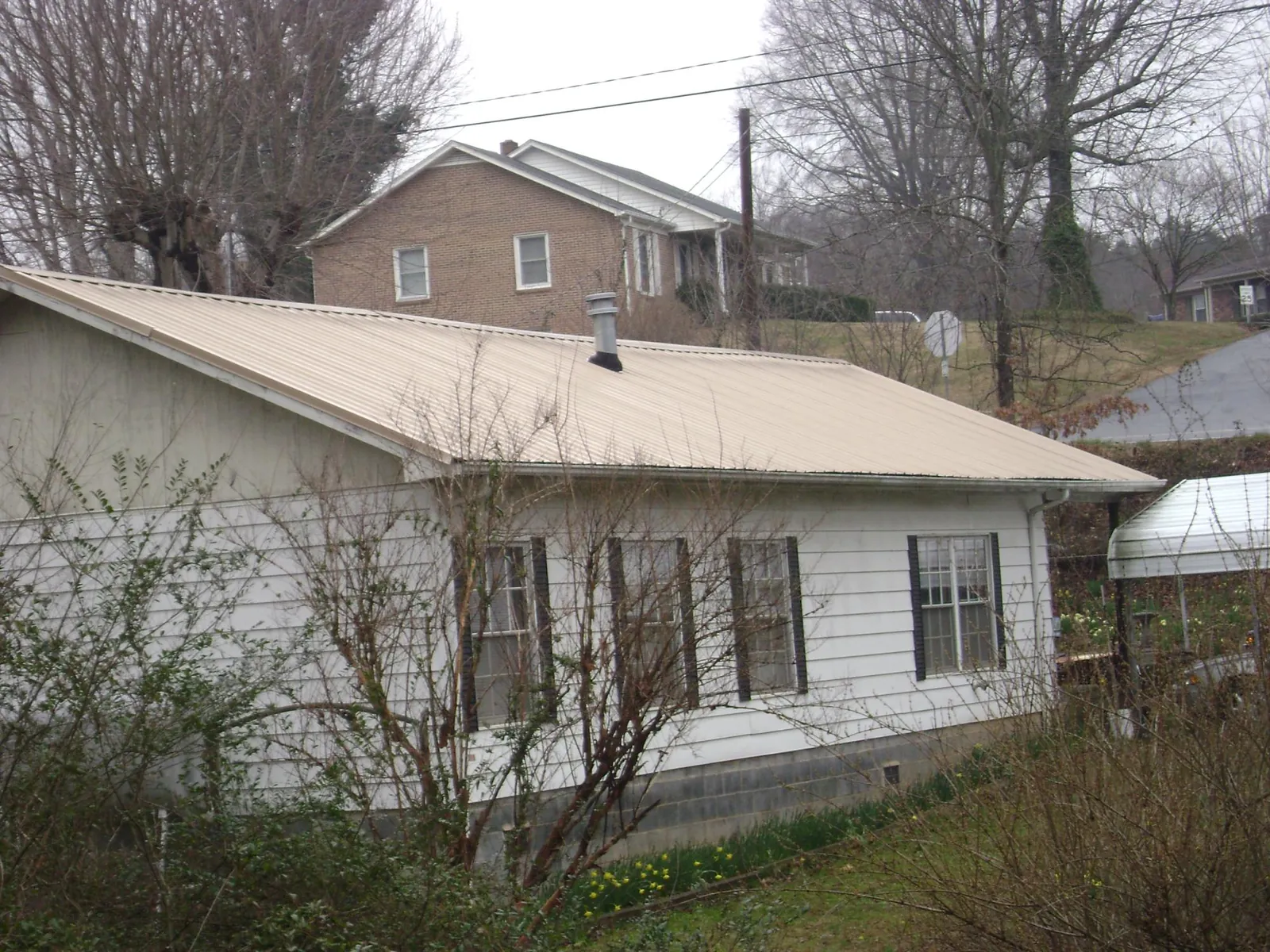 Tan metal roof on a white sided house set into a hillside — Commercial Roofing by Roofing Brothers in Ocean City